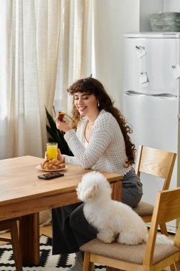 Genç bir kadın köpeğine gülümserken kruvasan ve meyve suyuyla keyifli bir kahvaltı yapar..