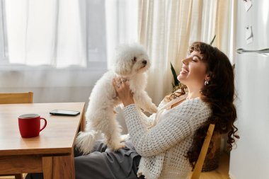 Genç bir kadın parlak bir odada tüylü köpeğiyle çay yudumluyor..