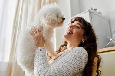 Genç bir kadın, parlak, davetkar bir uzayda tüylü beyaz köpeğini kucaklarken mutlulukla gülümsüyor..