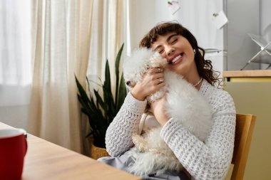 Genç bir kadın keyifle tüylü köpeğini sıcacık, bitki dolu bir odada kucaklıyor..