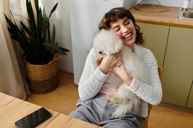 Kıvırcık saçlı genç bir kadın küçük beyaz köpeğiyle neşeli bir anı paylaşıyor..
