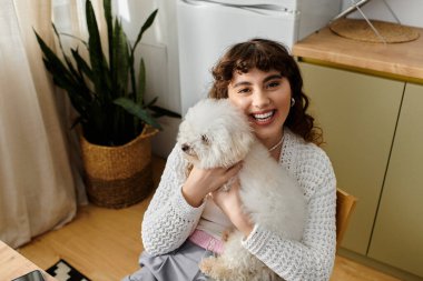 Genç bir kadın rahat bir atmosferde tüylü köpeğini kucaklarken neşeyle ışıldıyor..
