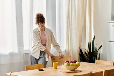 Gülümseyen genç kadın, içi taze meyve ve içecekle dolu, rahat, ahşap bir masada sandalyeler ayarlıyor..