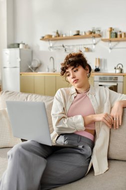 Parlak bir alanda, genç bir kadın rahat bir koltukta otururken dizüstü bilgisayarına odaklanır..