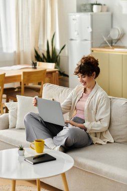 Genç bir kadın, parlak, davetkar bir yaşam alanında dizüstü bilgisayarı üzerinde çalışırken koltukta dinleniyor..