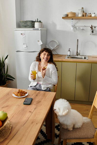 Молодая женщина наслаждается выпечкой за столом с игривой собакой поблизости утром.