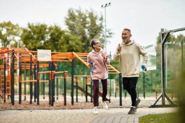 A loving couple runs hand in hand, laughing and enjoying the cool morning air at the park. clipart