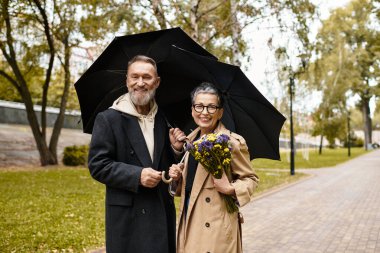 Sevgi dolu bir son sınıf çifti el ele yürür, huzurlu bir park ortamında gülümsemelerini ve çiçeklerini paylaşırlar..