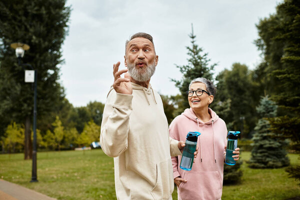 A loving couple walks hand in hand, sharing laughter and warmth in a serene park setting.