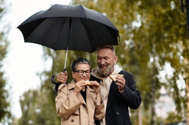 Sevgi dolu bir çift, yağmurdan korunurken, mutlu ve mutlu bir şekilde sandviçleri sever..