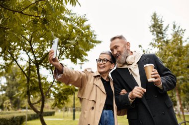 Sevgi dolu bir çift, güzel bir parkta yürürken gülücüklerini ve sıcaklıklarını paylaşarak selfie çeker..