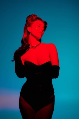 Şık giyinmiş genç bir kadın canlı bir arka plana karşı özgüvenle poz verir..