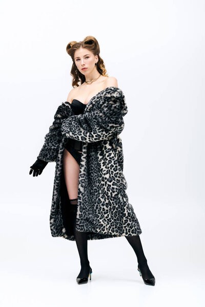 A young woman presents an alluring look in a leopard print coat, striking a fashionable pose.