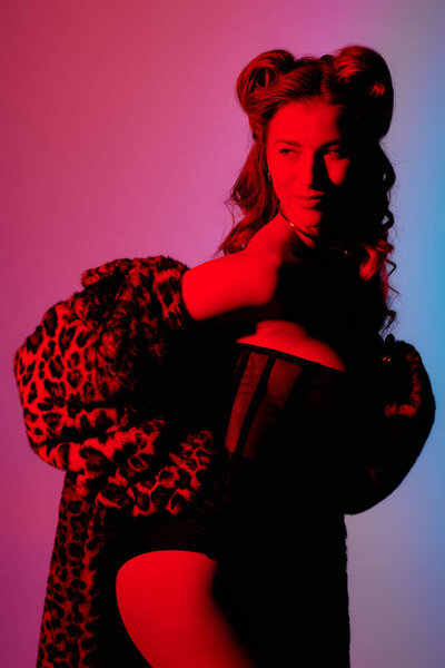 A young woman exudes confidence in a chic outfit, illuminated by vibrant, colorful lights.