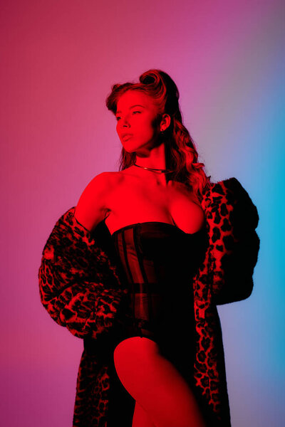 A stylish young woman flaunts her bold outfit under vibrant lights.
