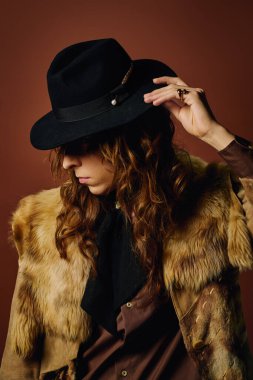 Yakışıklı genç bir adam şapkasını düzeltirken şık bir kürk mantosunu sıcak tonda sergiliyor..