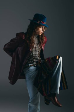 Genç bir adam, modern bir stüdyoda kendine güvenen, seçici bir kıyafet ve çarpıcı bir poz sergiliyor..