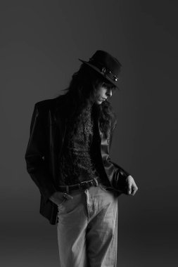 Yakışıklı bir genç adam kendine güvenerek duruyor, şık giyinmiş, karanlık bir arka plana karşı..