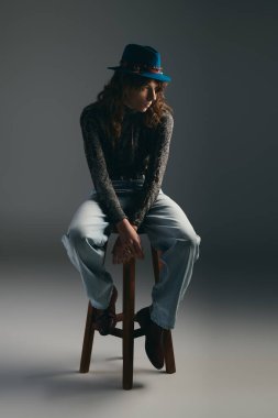 Genç, yakışıklı bir adam zarif bir şekilde bir taburede oturuyor, eşsiz bir moda ve dengeli bir zarafet sergiliyor..