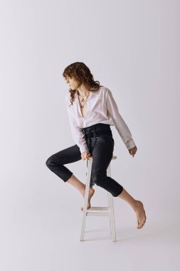 Yakışıklı genç bir adam beyaz bir taburede şık kıyafetler içinde poz verir..