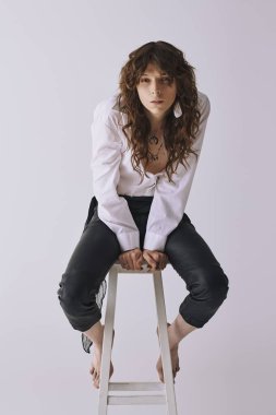 Şık bir genç adam minimalist bir arkaplana karşı taburede güven içinde poz verir..