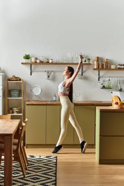 A young woman dances joyfully in her bright kitchen, feeling fit and happy. clipart