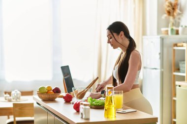 Spor sutyenli genç bir kadın güneşli bir mutfakta taze salata için sebze doğruyor..