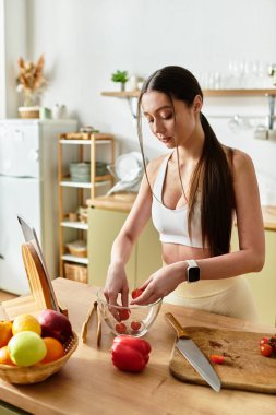 Spor sutyenli fit genç bir kadın şık mutfağında taze salata için sebze doğruyor..
