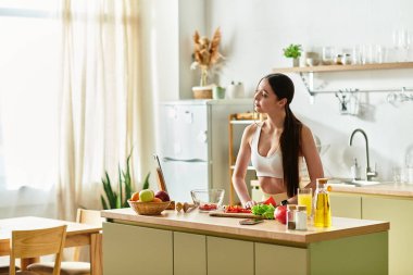 Geniş bir mutfakta, spor sutyenli sağlıklı bir kadın neşeyle sağlıklı bir salata hazırlar..