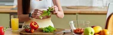 Spor sutyenli, formda genç bir kadın renkli sebzeli taze bir salata hazırlıyor.
