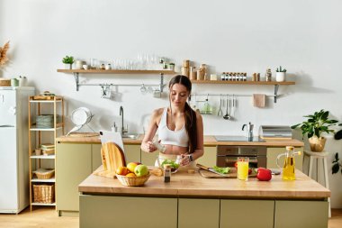 Spor kıyafetli fit bir kadın şık bir mutfakta canlı malzemelerle taze salata yapar..