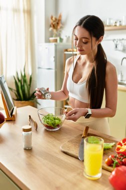 İyi ışıklandırılmış bir mutfakta, spor sutyenli fit bir kadın, canlı bir salata hazırlar..