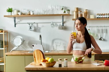 Spor sütyenli genç bir kadın canlandırıcı bir içecek içerken canlı bir salata hazırlıyor..