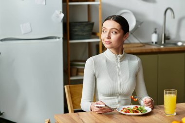 Genç bir kadın, mutfağında salata ve meyve suyu bulunan sağlıklı bir kahvaltıdan hoşlanır..