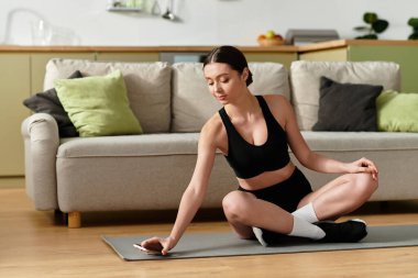 Siyah spor kıyafetli genç bir kadın modern bir dairede egzersiz yapıyor..