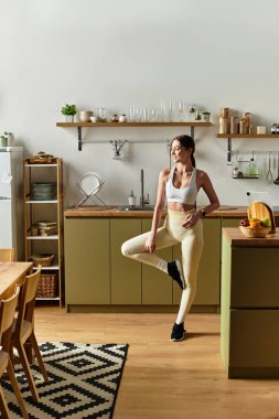 Güzel, genç bir kadın modern mutfağında neşeyle dans ediyor. Fitness ve mutluluğu ifade ediyor..