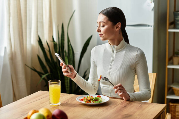 A young woman savors a healthy breakfast while checking her phone in a bright kitchen.