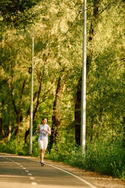 A young beautiful woman enjoys a refreshing jog along a winding path in a lush forest setting. clipart