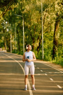 Sportif bir kadın, güneşli bir günde kendine güvenerek içkisini yudumlar ve doğanın tadını çıkarır..