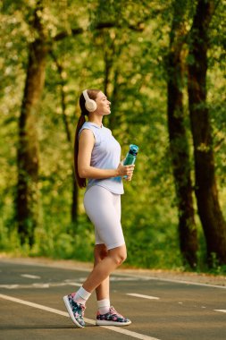 Genç, atletik bir kadın canlı bir parkta huzur içinde yürüyor. Doğası gereği güzelliğe dalmış..