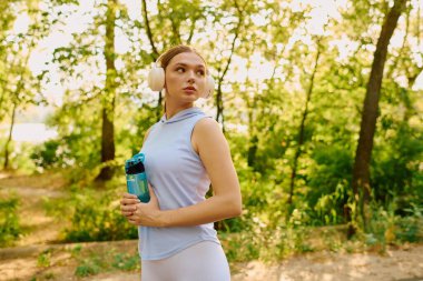 Kendine güvenen genç bir kadın zarif bir şekilde elinde bir su şişesiyle durup müzik dinliyor..