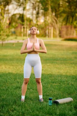 Gür yeşil bir parkta, güzel bir atletik kadın yoga yapıyor, sükuneti kucaklıyor ve odaklanıyor..
