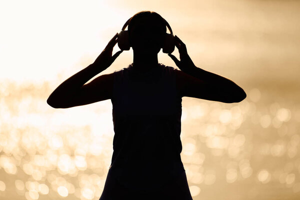 A young athletic woman by the water enjoys the peaceful sunset with headphones on.