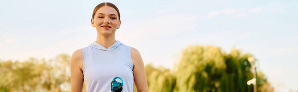 A beautiful athletic woman stands outdoors with a smile, ready for her outdoor workout routine.