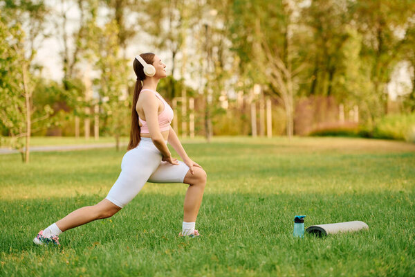 A beautiful and athletic young woman stretches gracefully in a lush green park, embracing nature.