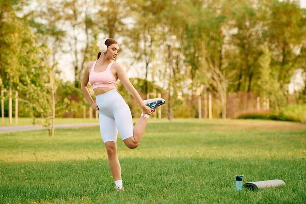 A fit young woman stretches her leg while exercising in a vibrant green park.