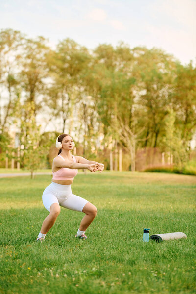 A beautiful athletic woman is exercising in a green park during a bright sunny day, staying fit.