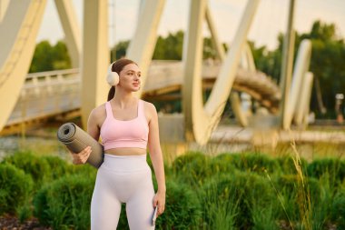 Genç atletik kadın kendine güvenen yoga minderiyle su kenarında akşam egzersizi için hazır bekliyor..