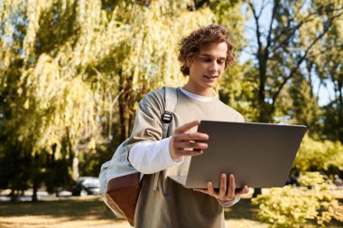 Genç adam güneşli bir parkta dizüstü bilgisayarıyla meşgul. Etrafı renkli sonbahar yapraklarıyla çevrili..