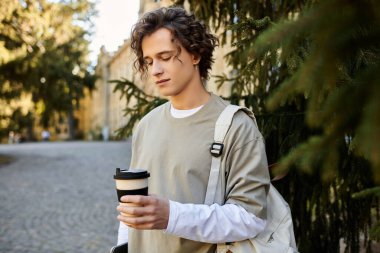 Yakışıklı öğrenci, büyüleyici bir üniversite ortamında gezinirken sıcak bir içkinin tadını çıkarıyor..